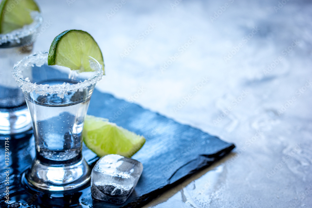 Alcohol shots with ice, lime and salt on gray stone background