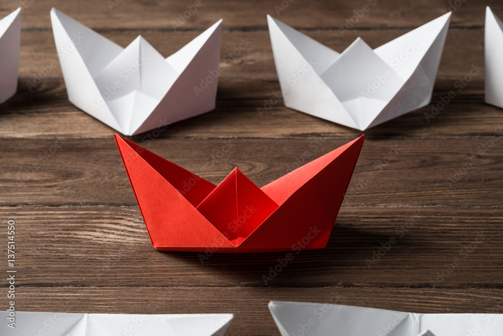 Business leadership concept with white and color paper boats on wooden table