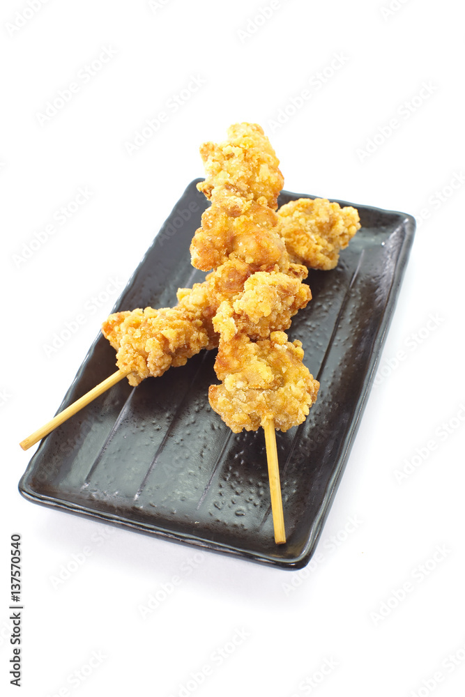 Crispy deep fried chicken with skewer and black plate on white background