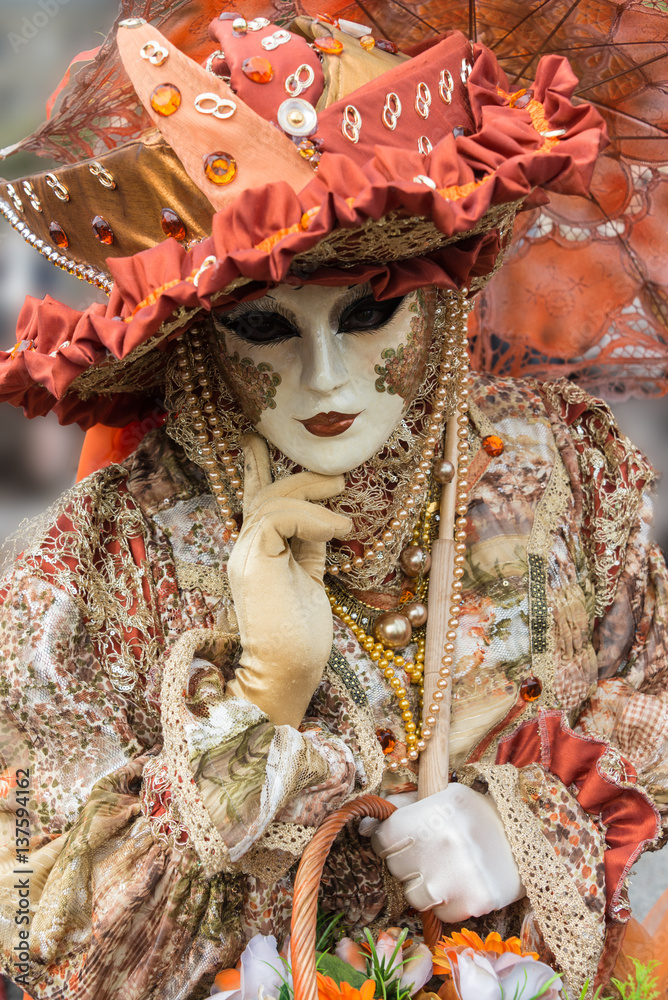 Masque de venise et costume de carnaval. Ton beige et orange. Masque blanc et doré. Regard triste.