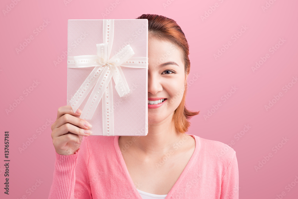 Pretty asian young woman holding gift on pink background.