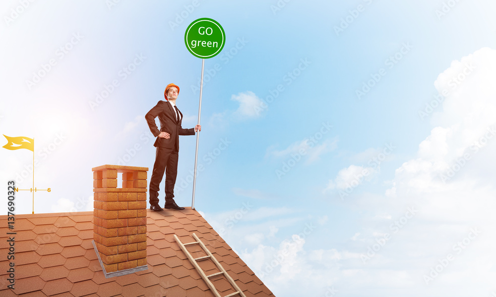 Businessman in suit on house top with ecology concept signboard. Mixed media