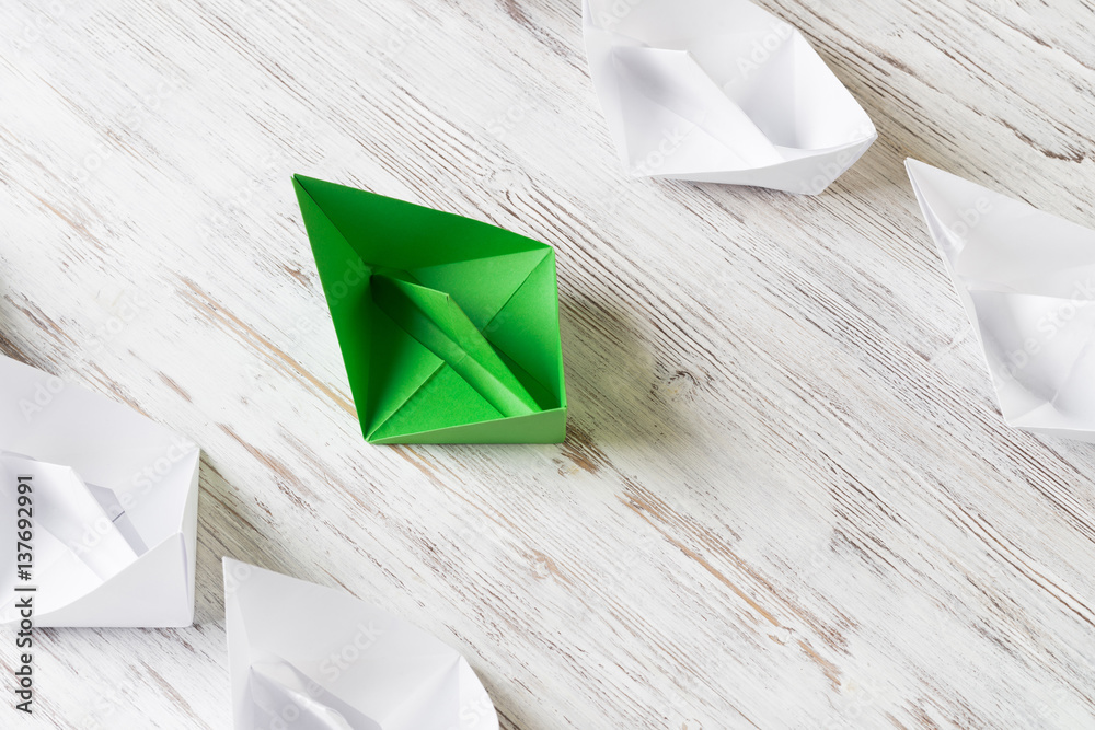 Business leadership concept with white and color paper boats on wooden table