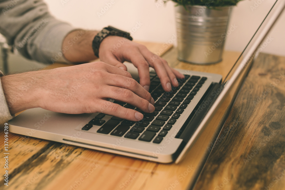 Closeup of male hands typing on laptop keyboard in modern office