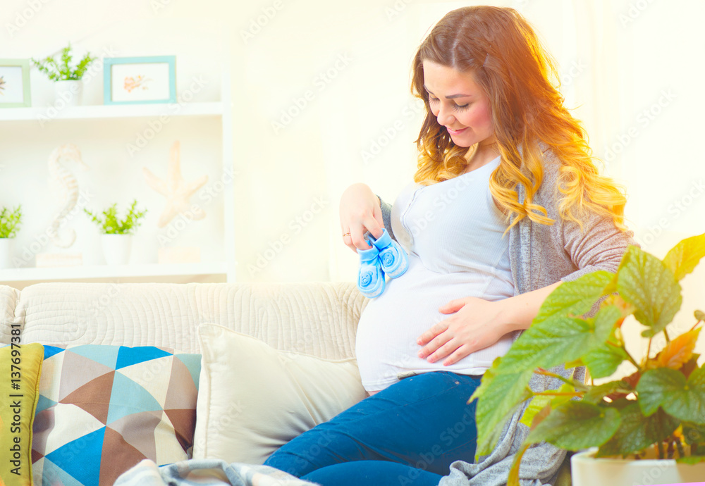 Pregnant happy woman holding blue baby shoes in her hands