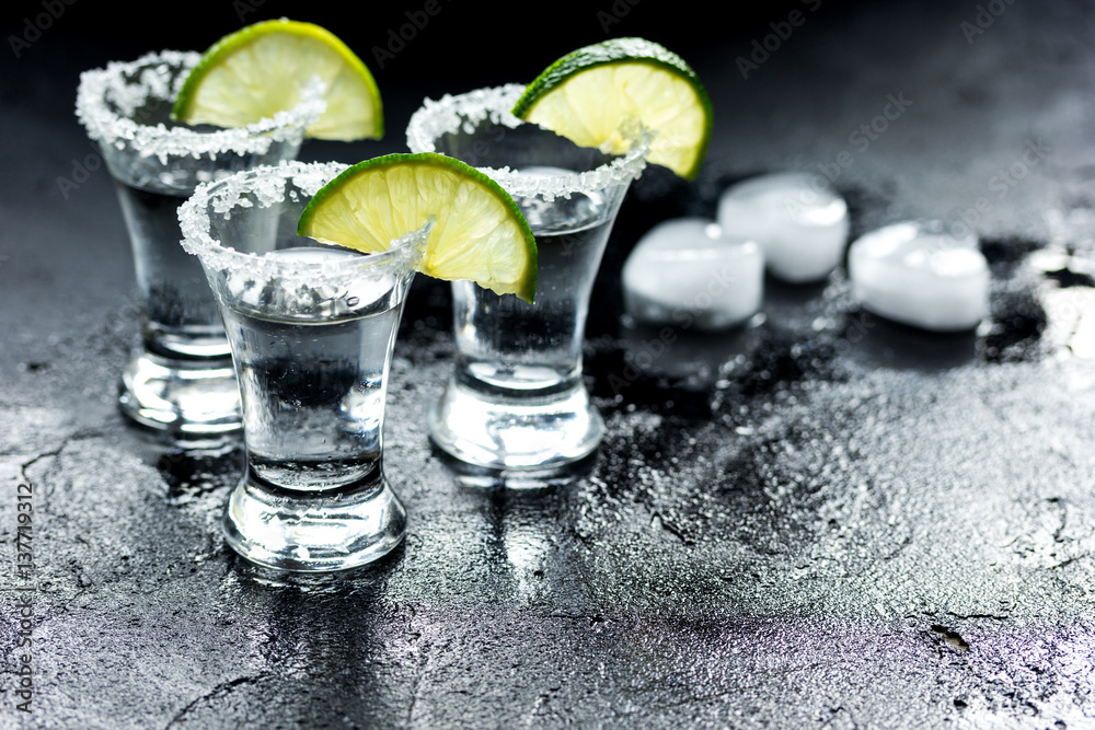 Tequila shot with lime slices and salt on dark background