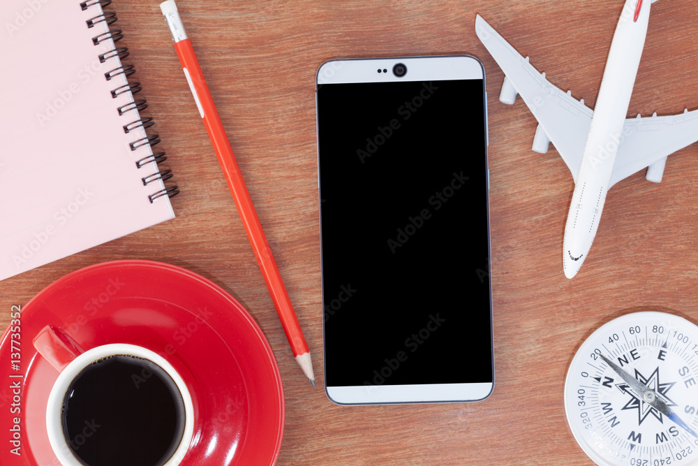 Red coffee cup with smartphone ,paper note ,airpland model,compass and pencil on wood table backgrou