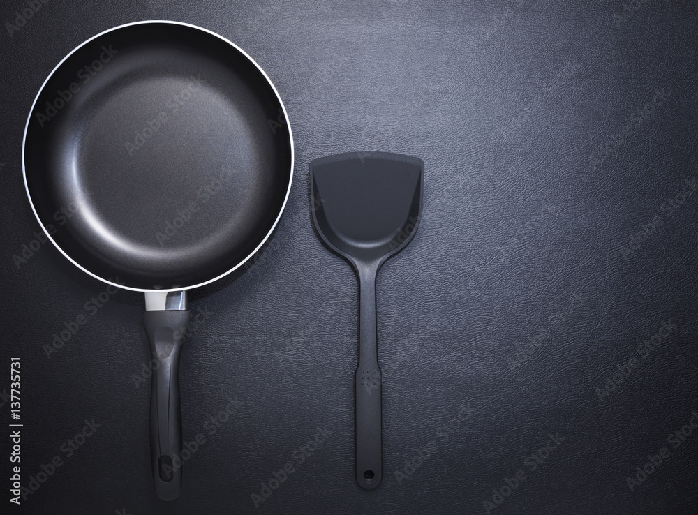 Top view frying pan and plastic spade on black table background.