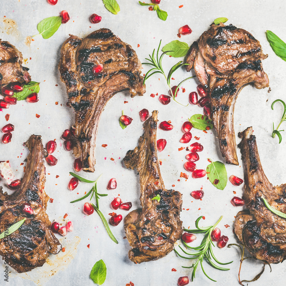 Grilled lamb ribs with pomegranate seeds, fresh mint and rosemary over metal baking tray background,