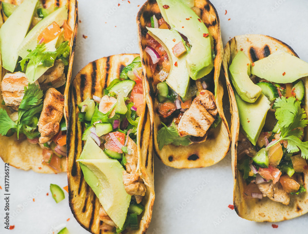 Healthy corn tortillas with grilled chicken fillet, avocado, fresh salsa, limes over light grey marb