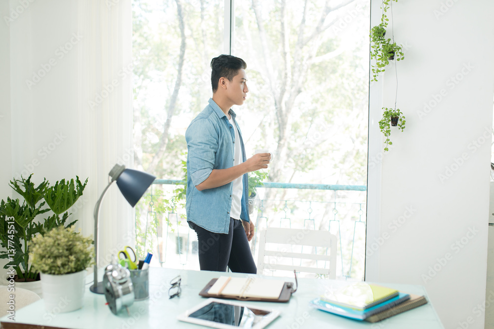 Thoughtful asian man looking out the window in bedroom at home