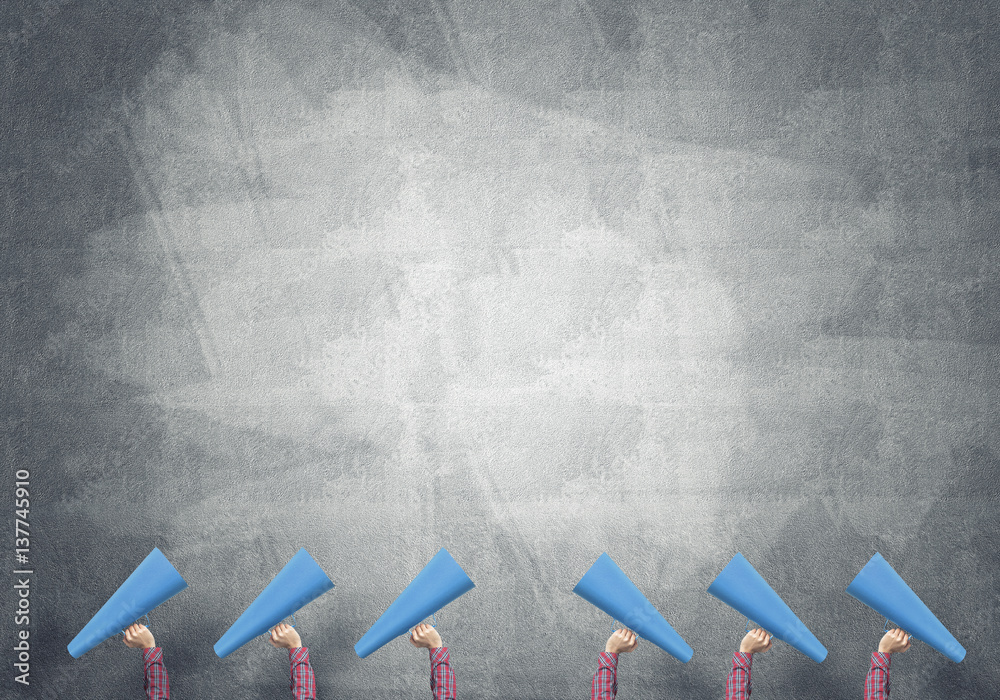 Many hands of woman holding paper trumpet against concrete background