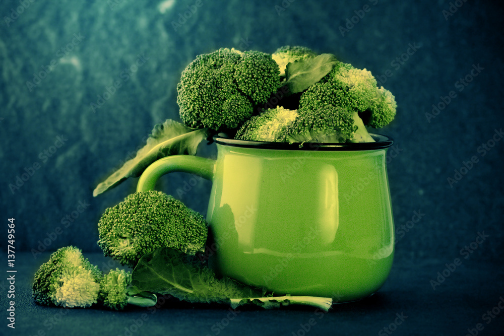 still life with fresh green broccoli in ceramic cup on black stone plate