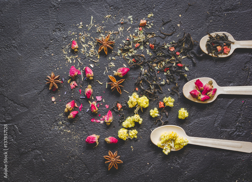 Spoons with herbs on dark background top view