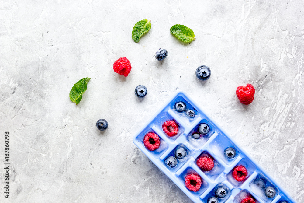 Ice tray with berries and mint on stone top view mock up