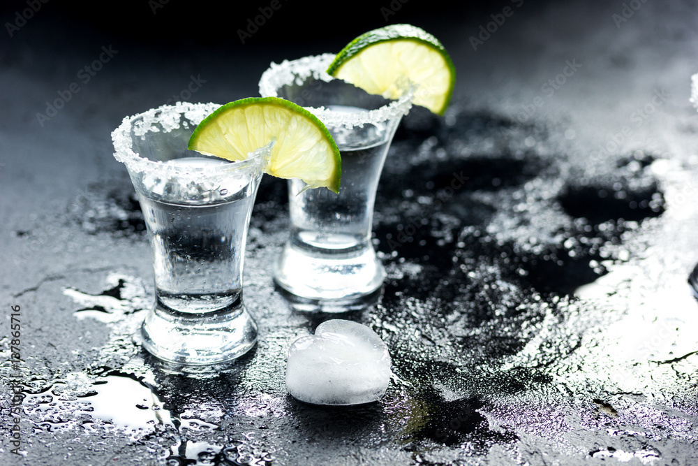 Tequila shot with lime slices and salt on dark background