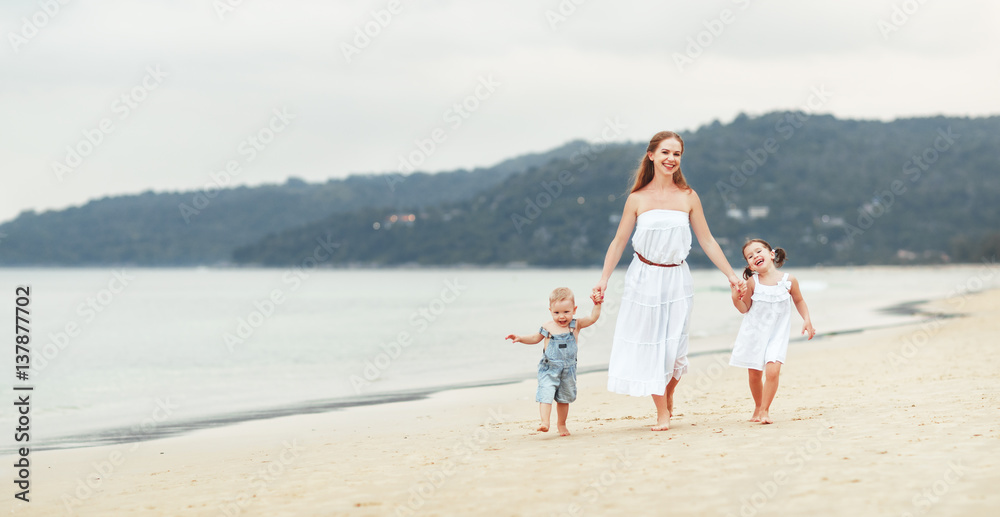 Happy family mother and children on beach by sea in summer