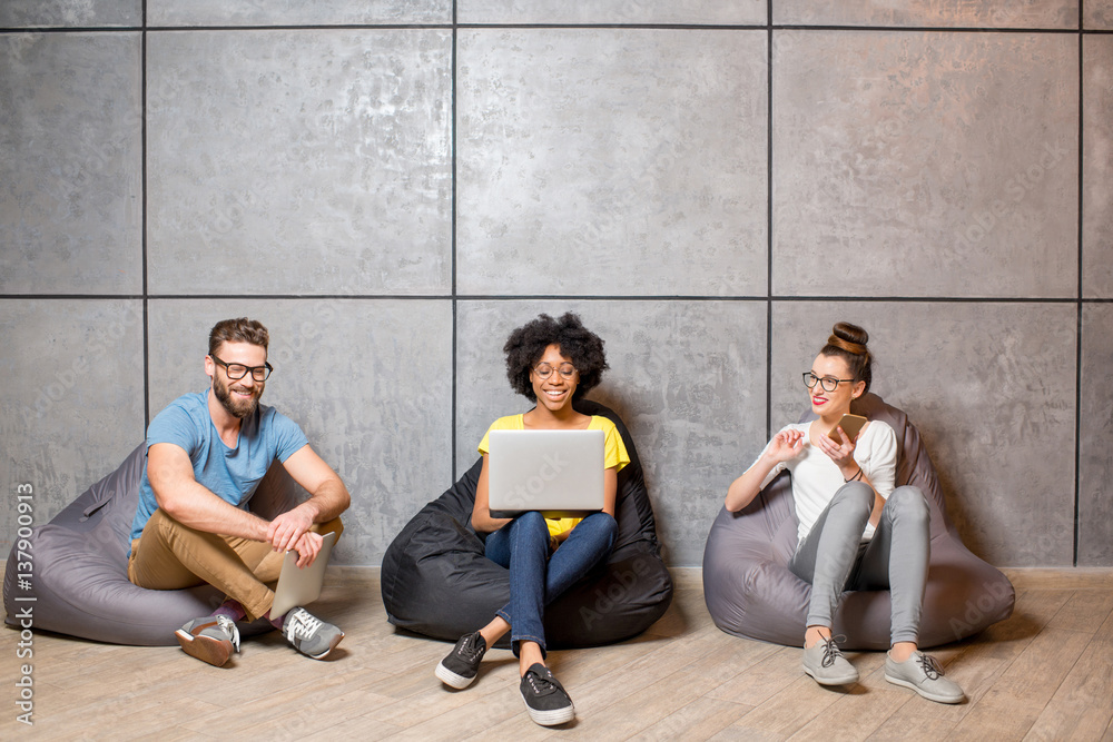 Multi ethnic coworkers dressed casually in colorful clothes working with different gadgets sitting o