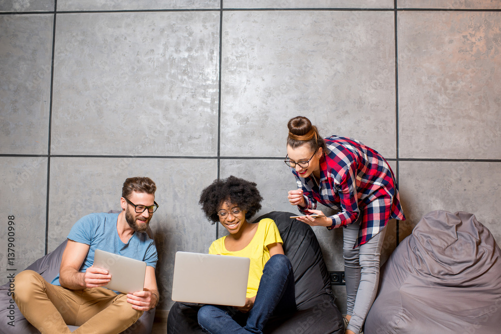 Multi ethnic coworkers dressed casually in colorful clothes working together with different gadgets 