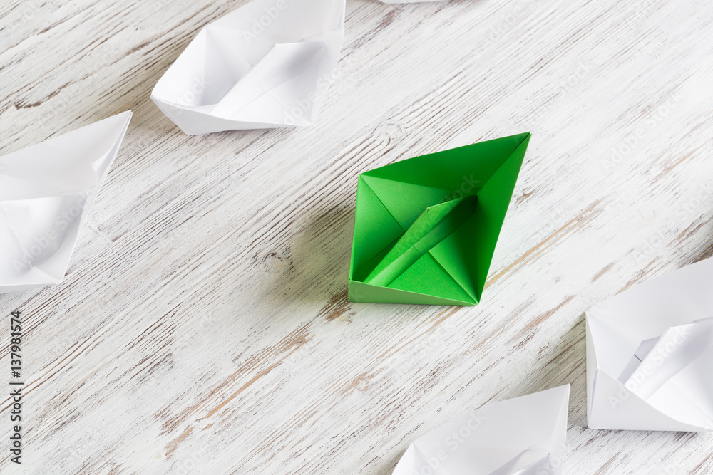 Business leadership concept with white and color paper boats on wooden table