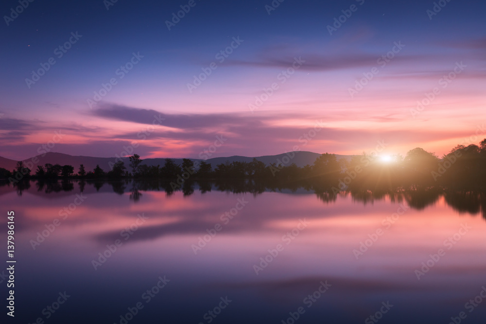 Mountain lake with moonrise at night. Night landscape with river, trees, hills, moon and colorful pu