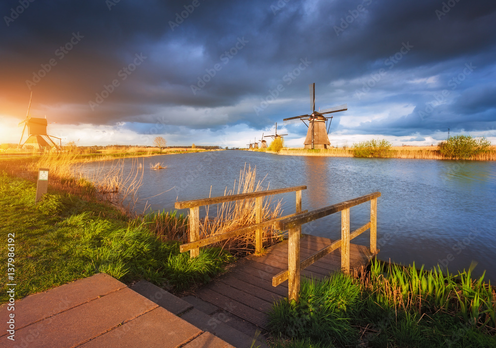 Windmills at sunset in Kinderdijk, Netherlands. Rustic landscape with wooden pier against amazing du