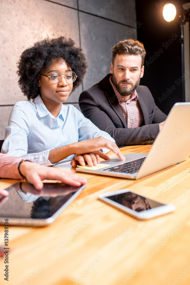 Beautiful african woman with handsome caucasian man working with laptop at the modern office interio