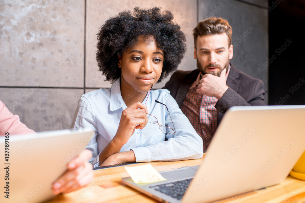 Beautiful african woman with handsome caucasian man working with laptop at the modern office interio