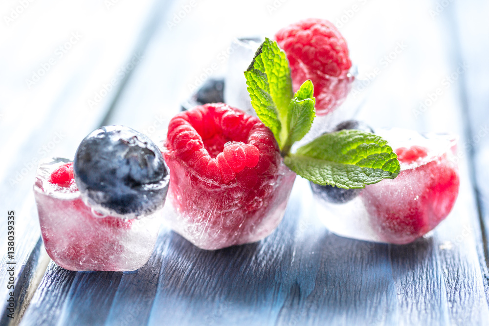 fresh berries with mint in ice cubes on wooden background