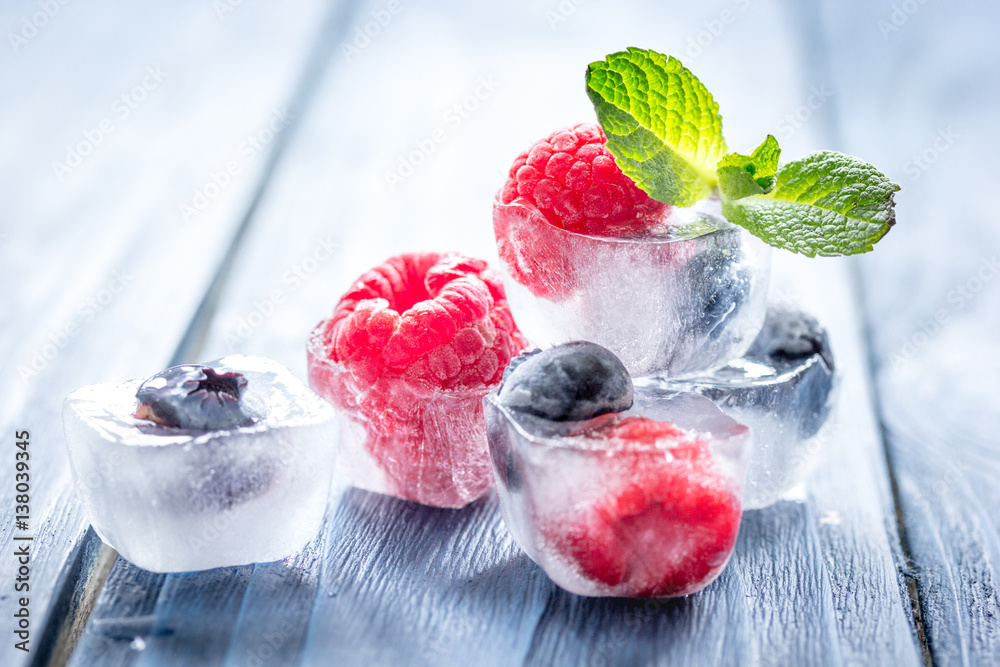 fresh berries with mint in ice cubes on wooden background