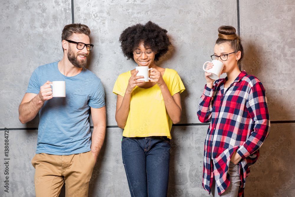 Multi ethnic coworkers dressed casually having a coffee break near the gray wall indoors