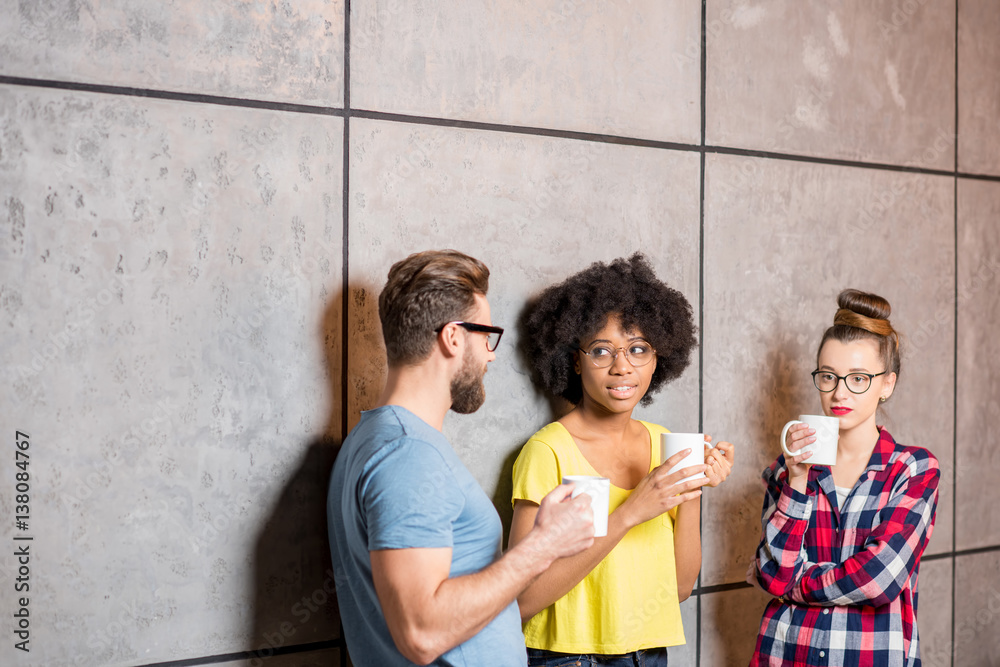 Multi ethnic coworkers dressed casually having a coffee break near the gray wall indoors