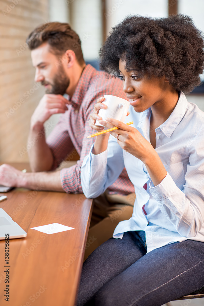 Beautiful african businesswoman and caucasian man working together with laptops and coffee cups near