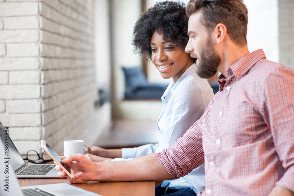 Beautiful african businesswoman and caucasian man working together with laptops and smart phone near