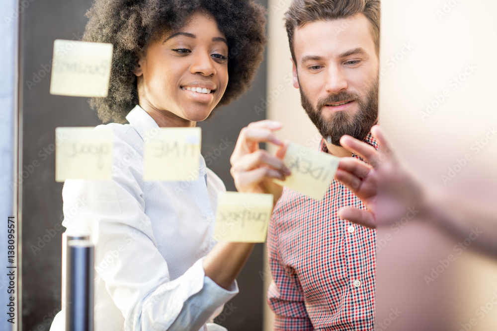 Multi ethnic coworkers working together with stickers on the transparent door at the office