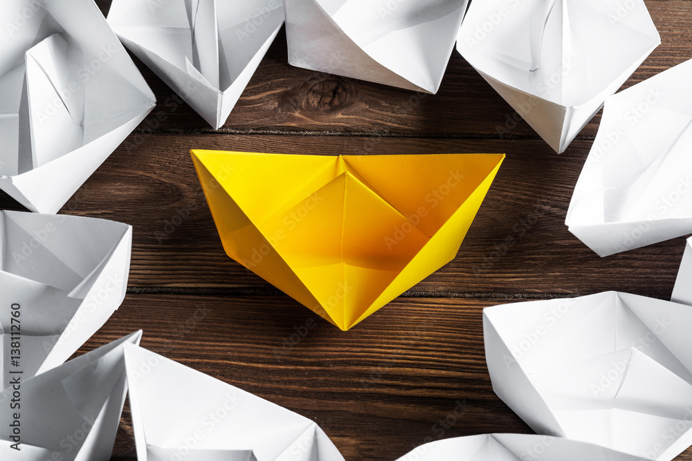 Business leadership concept with white and color paper boats on wooden table