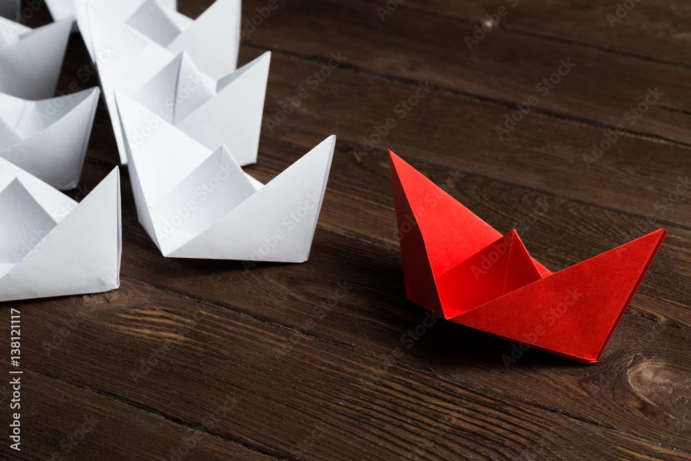 Business leadership concept with white and color paper boats on wooden table