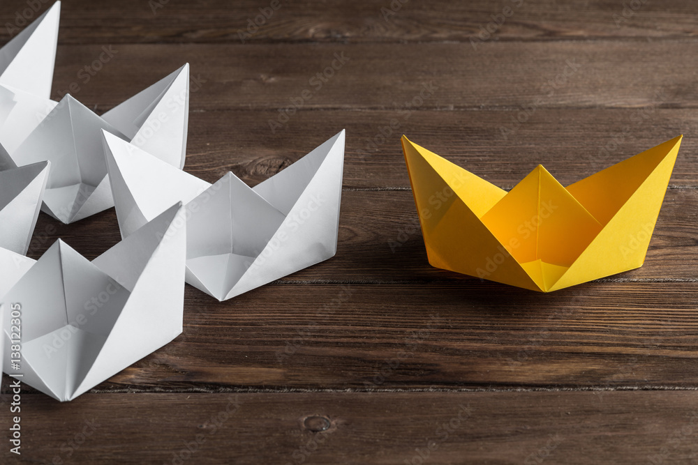 Business leadership concept with white and color paper boats on wooden table