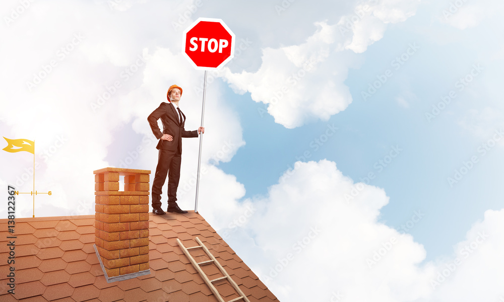 Caucasian businessman on brick house roof showing stop road sign. Mixed media