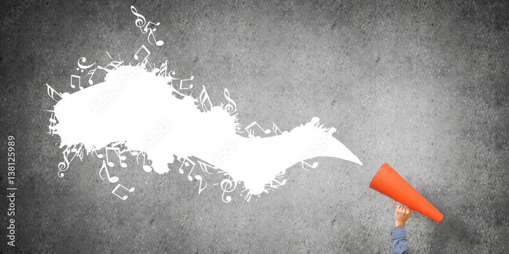 Hand of man holding orange paper trumpet against concrete background