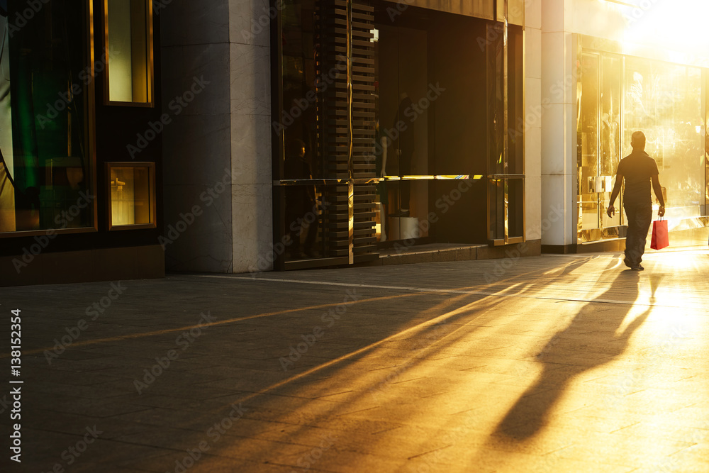 A shopper walking past a store window at sunrise in the shopping street .