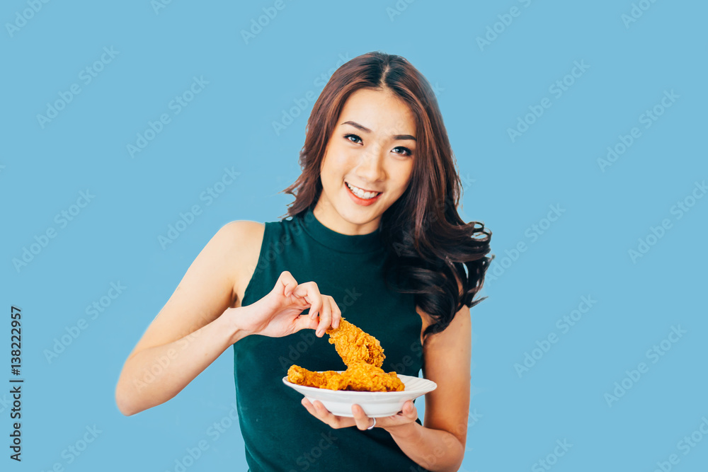 Attractive Asian woman eating fried chicken drumstick over white brick background