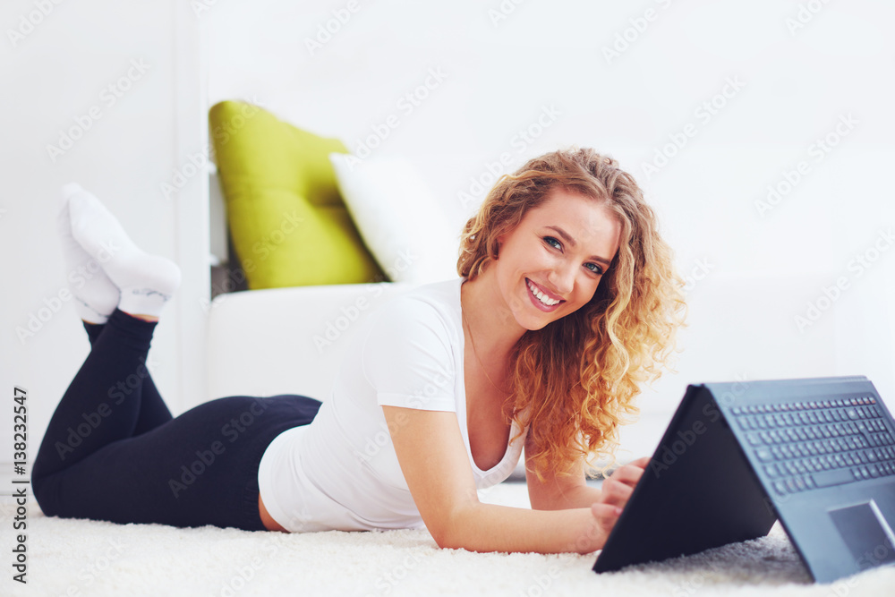 happy young woman working with laptop, lying on carpet at home