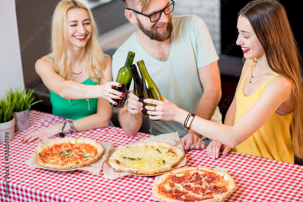 Young friends dressed casually in colorful t-shirts having lunch with pizza and beer at home