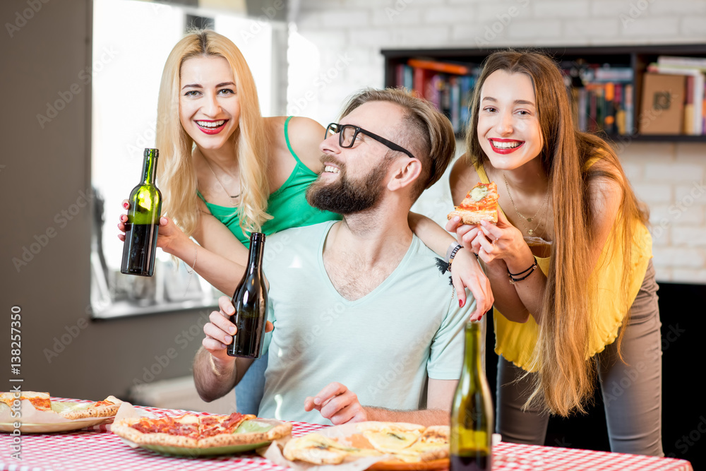 Young friends dressed casually in colorful t-shirts having fun eating pizza and drinking beer at hom