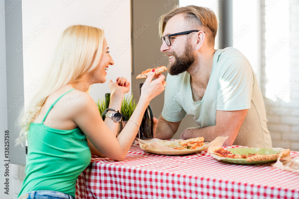 Young couple dressed casually having a lunch with pizza and beer at home