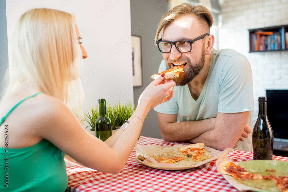 Young couple dressed casually having a lunch with pizza and beer at home