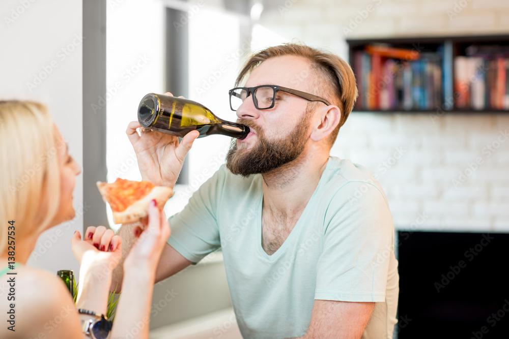 Young couple dressed casually having a lunch with pizza and beer at home