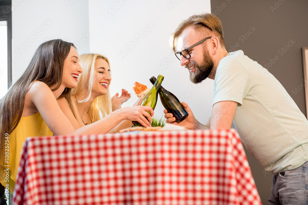 Young friends dressed casually in colorful t-shirts having lunch with pizza and beer at home