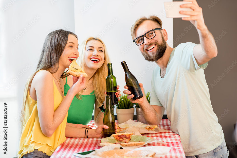 Young friends dressed casually in colorful t-shirts making selfie photo with pizza and beer at home